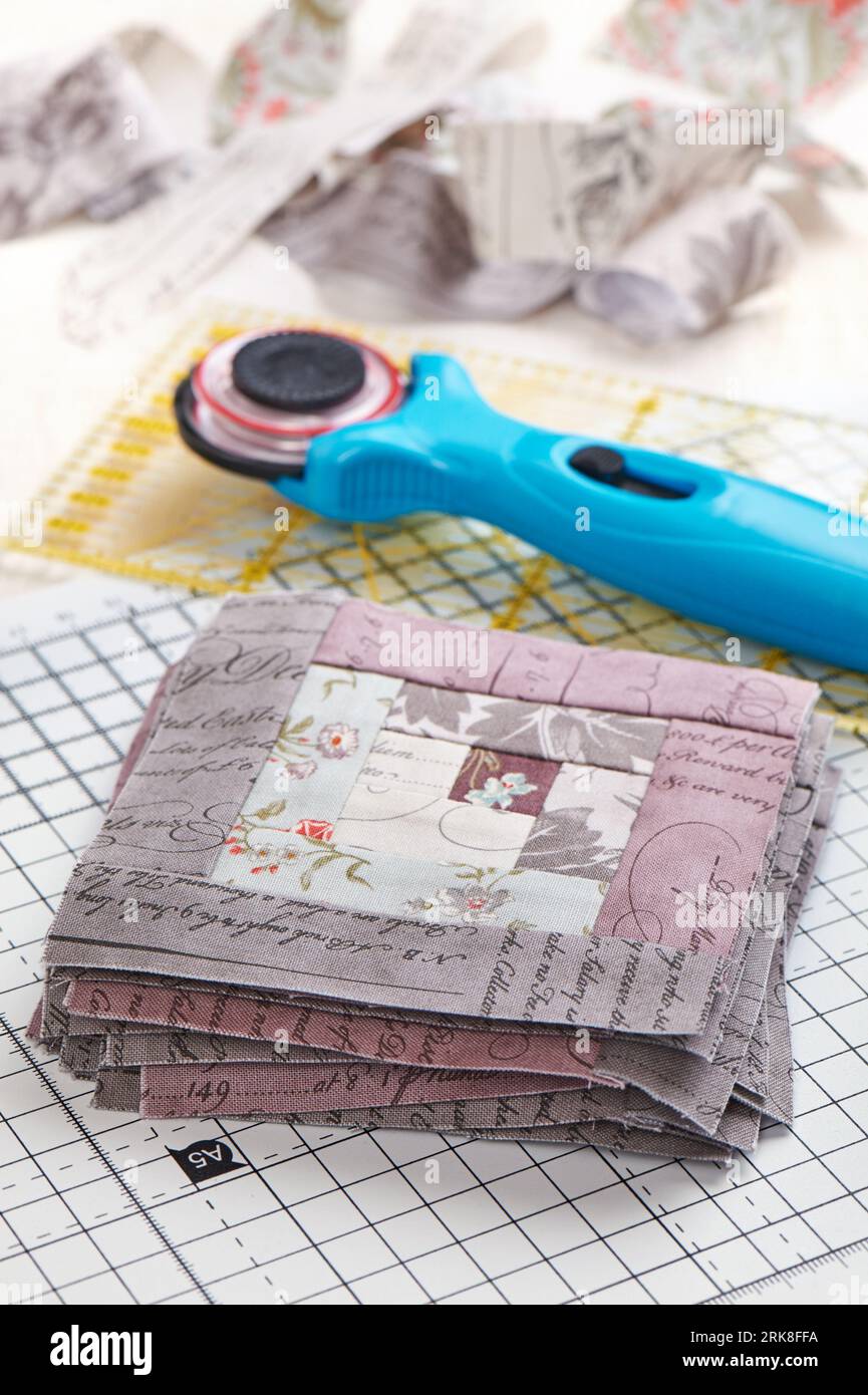 Patchwork log cabin blocks on craft mat, stack of blocks, sewing accessories on white wooden surface Stock Photo