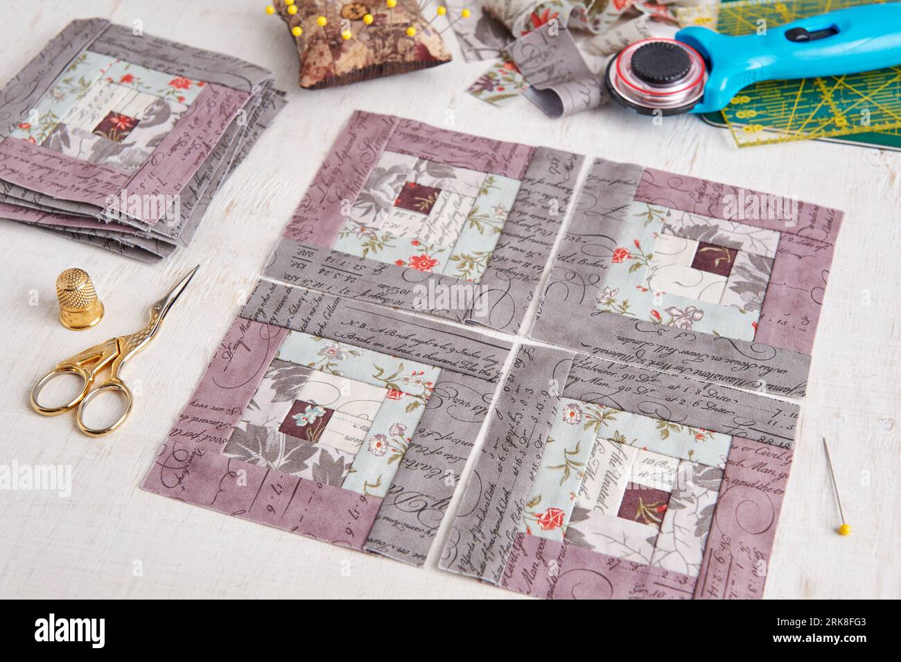Patchwork log cabin blocks, stack of blocks, sewing accessories on white wooden surface Stock Photo
