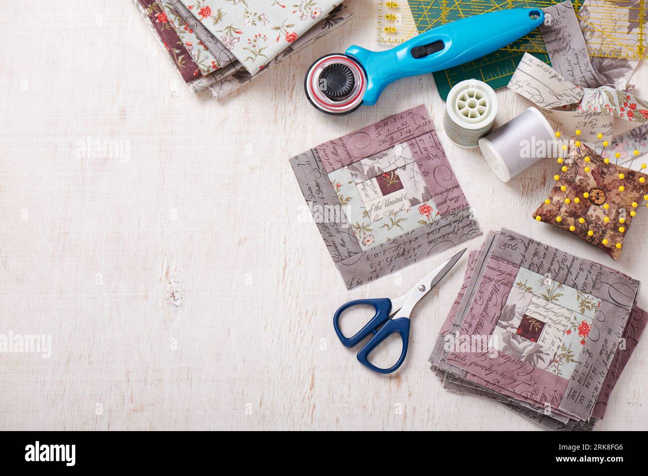 Patchwork log cabin blocks, stack of blocks, sewing accessories on white wooden surface Stock Photo