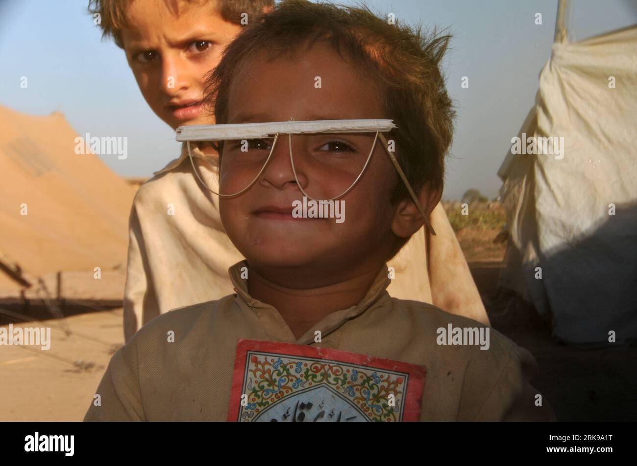 Bildnummer: 54155910  Datum: 19.06.2010  Copyright: imago/Xinhua (100620) -- ISLAMABAD, June 20, 2010 (Xinhua) -- An Afghan boy wears a pair of glasses made by himself at a refugee camp on the suburbs of Islamabad, capital of Pakistan, June 19, 2010. The United Nations marks the World Refugee Day on Sunday with the theme of Home by reminding the world of the 15 million refugees who are unable to return to their homes. (Xinhua/Yan Zhonghua) (wjd) (5)PAKISTAN-AFGHANISTAN-REFUGEE PUBLICATIONxNOTxINxCHN Gesellschaft kbdig xkg 2010 quer premiumd xint o0 Kind Junge Flüchtling Brille selbstgemacht Stock Photo
