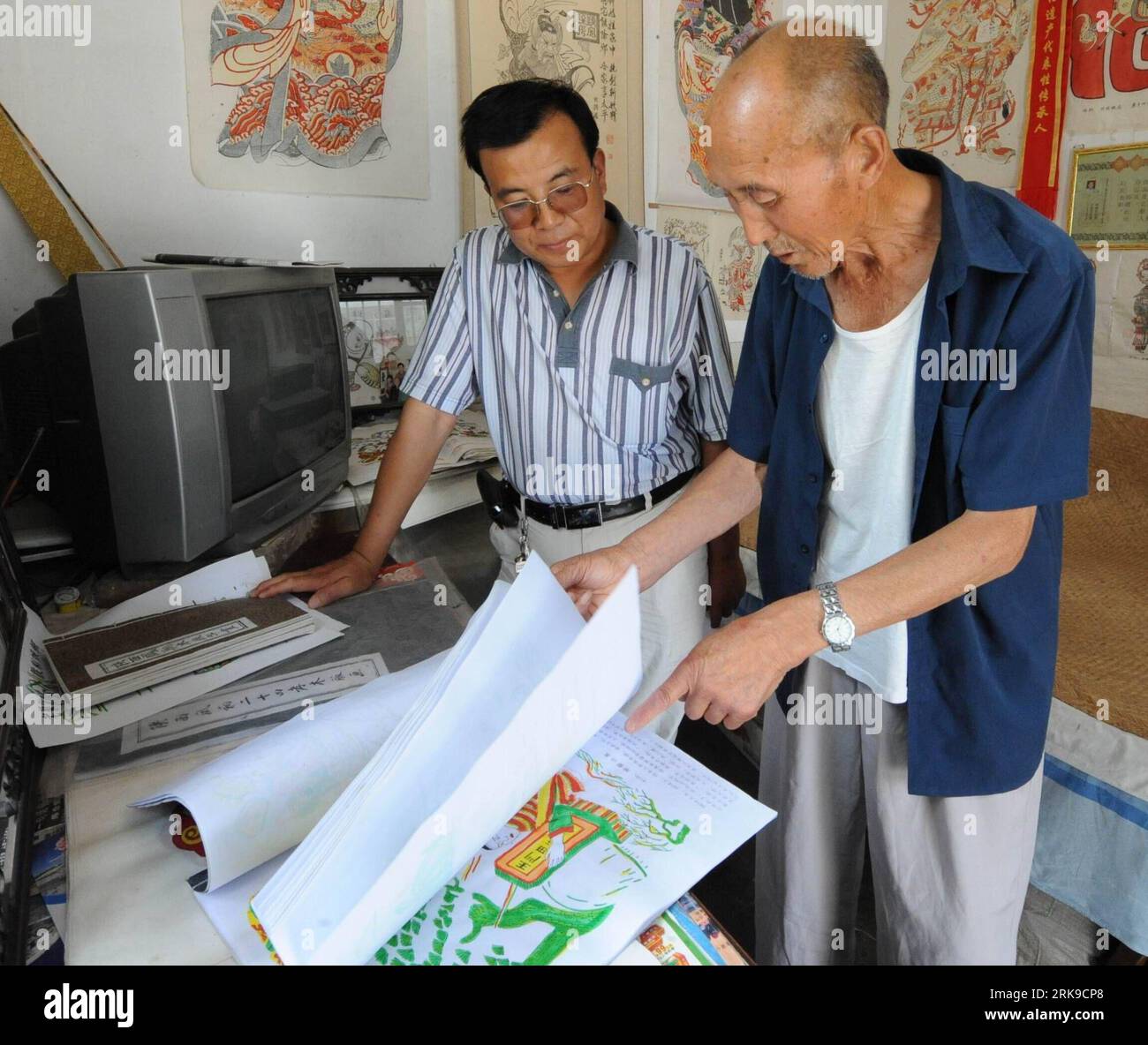 Bildnummer: 54168698  Datum: 24.06.2010  Copyright: imago/Xinhua Xi an, June 24, 2010 (Xinhua) -- Folk artist Tai Yu (R) shows his woodcut prints painting book at his studio in Fengxiang County of Baoji City, northwest China s Shaanxi Province, June 24, 2010. The 77 years old folk artist Tai Yu learnt the skills of making spring festival woodcut prints when he was a kid. Through his more than 60 years practices in woodcut prints Tai inherited traditional skills from ancestor artists and drew inspirations form stone carving, paper-cutting, and embroidering and formed his own style. His woodcut Stock Photo