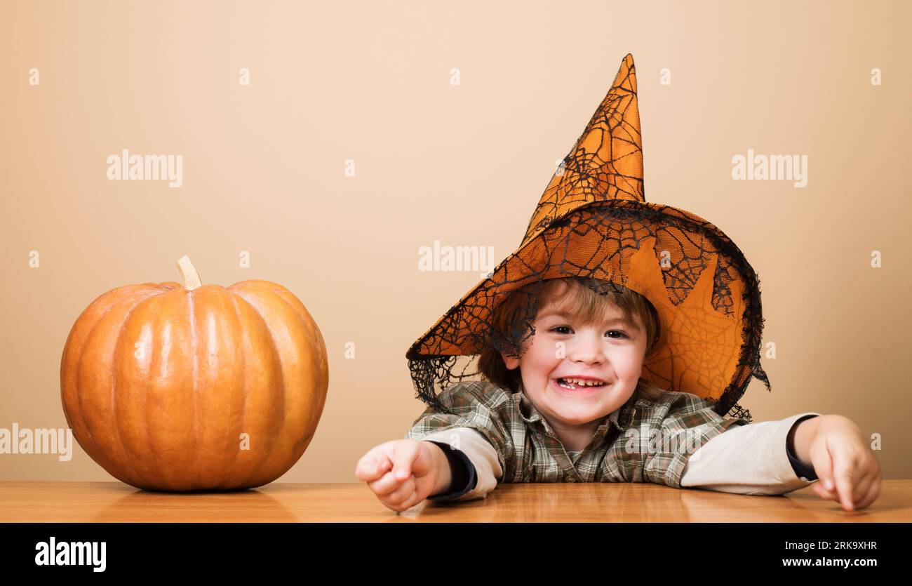 Happy Halloween. Smiling kid boy in witch hat with magic pumpkin. Funny child in witch hat for Halloween with pumpkin Jack. Little kid in wizards Stock Photo