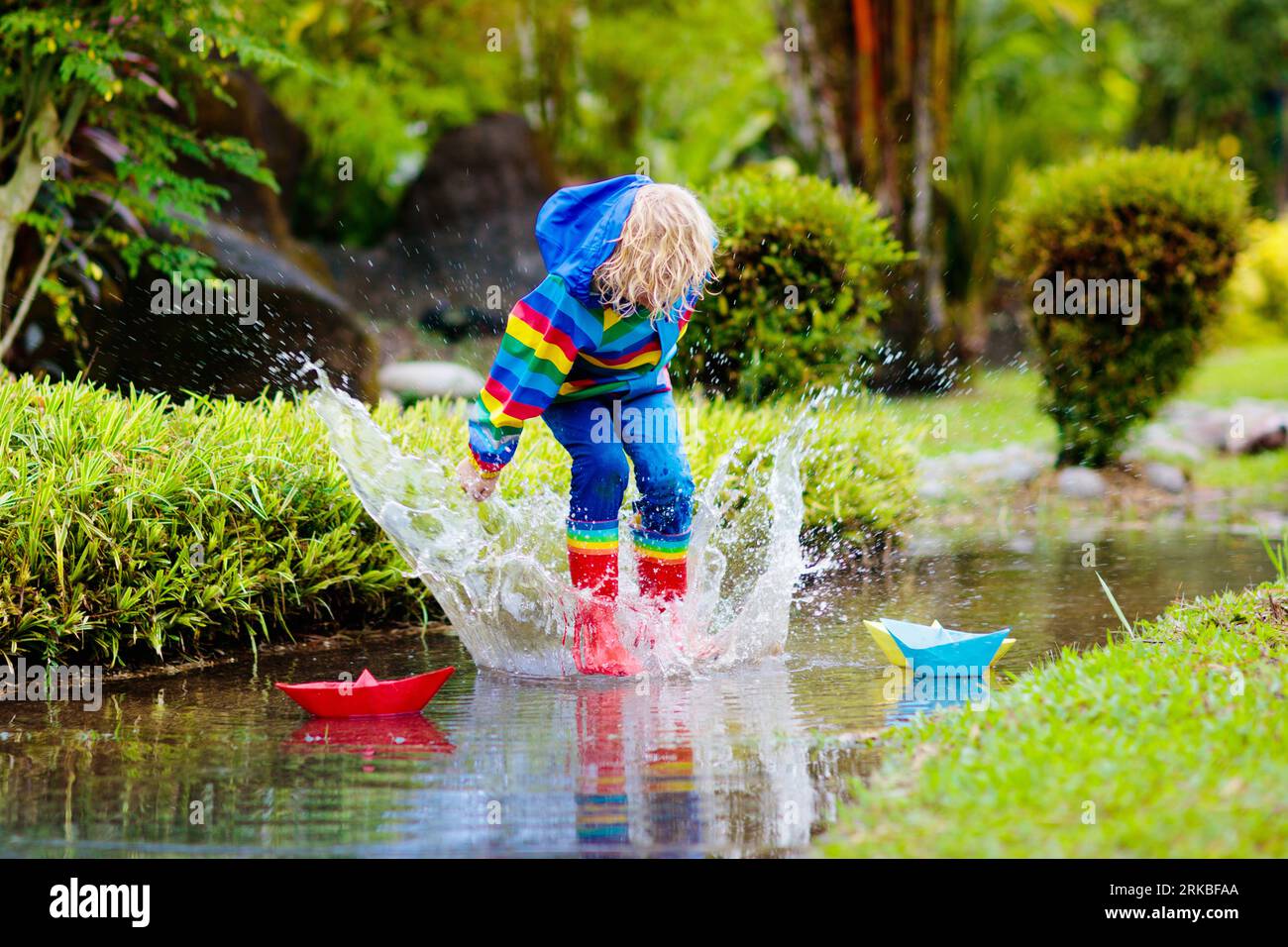 Child playing with paper boat in puddle. Kids play outdoor by autumn ...