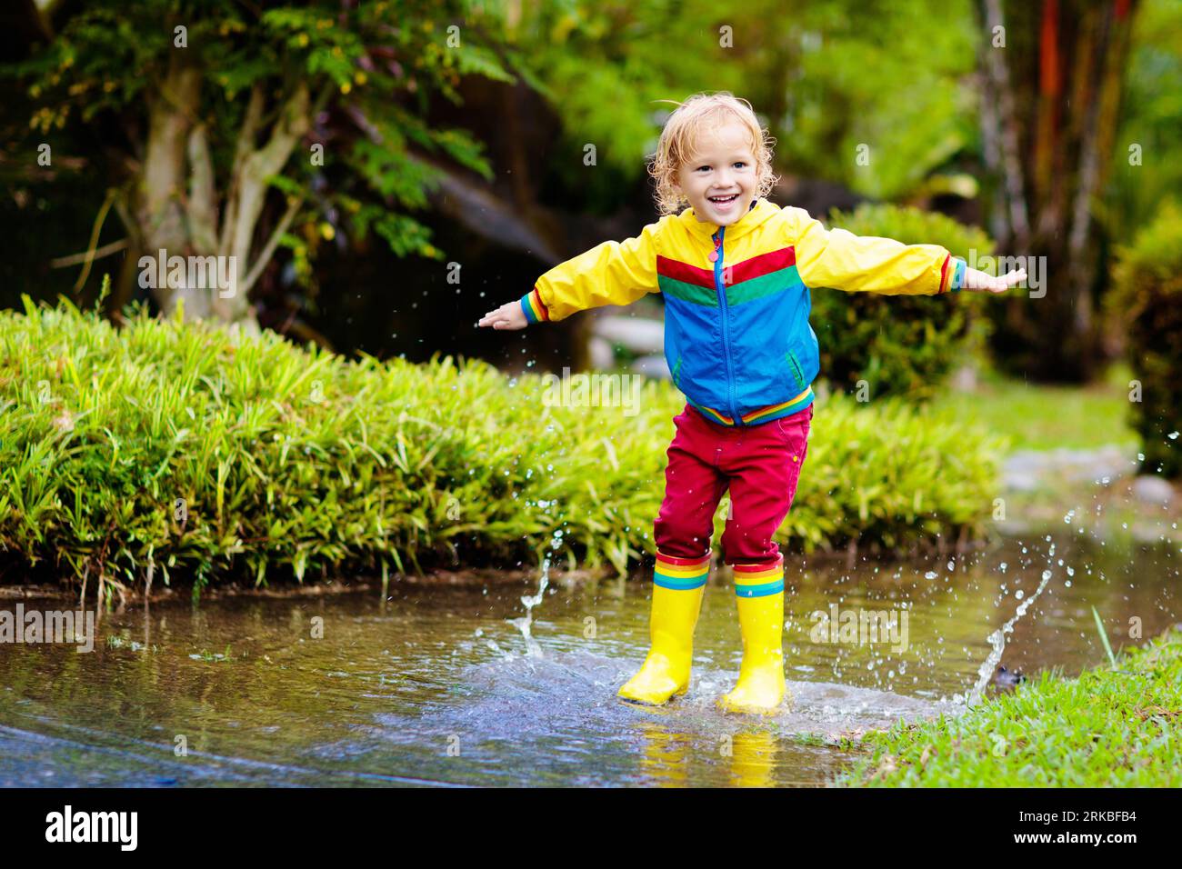 Child playing in puddle. Kids play and jump outdoor by autumn rain ...