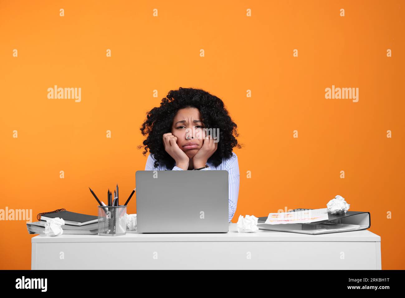 Stressful deadline. Exhausted woman sitting at white desk against orange background Stock Photo