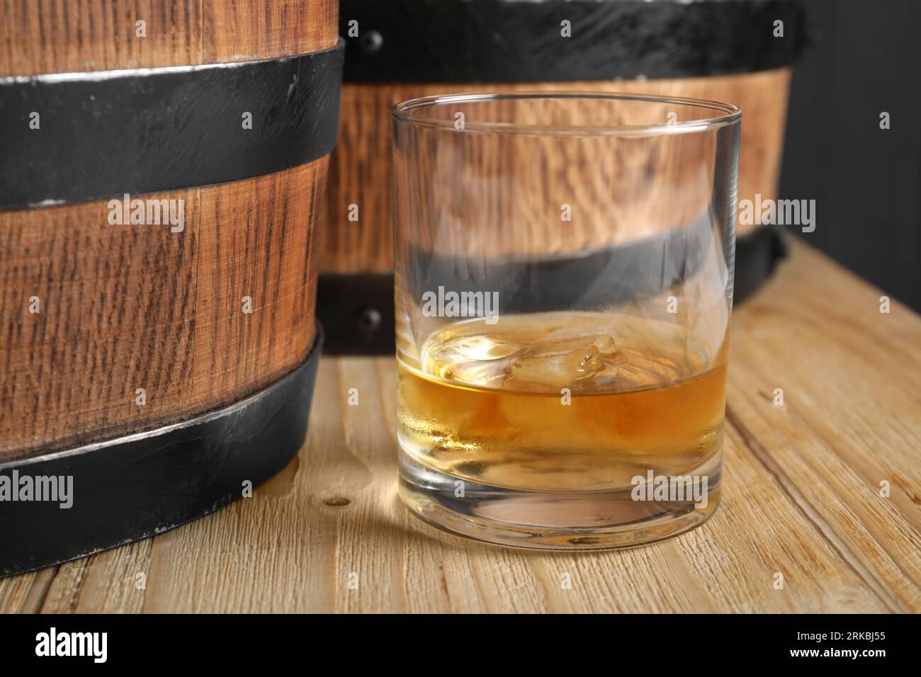 Barrels and glass of tasty whiskey on wooden table, closeup Stock Photo