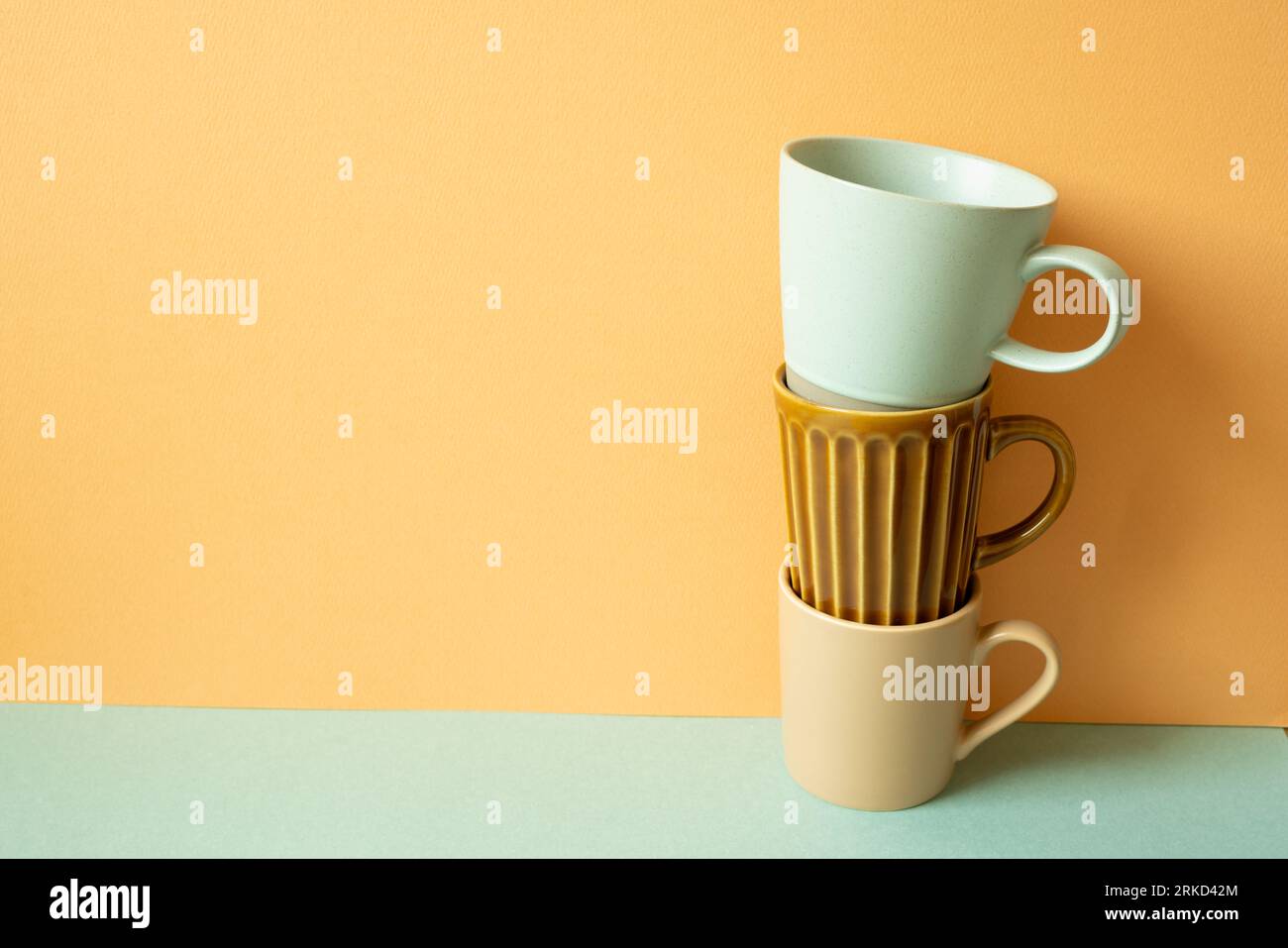 Stack of mug cup on mint green table. orange wall background. copy space Stock Photo