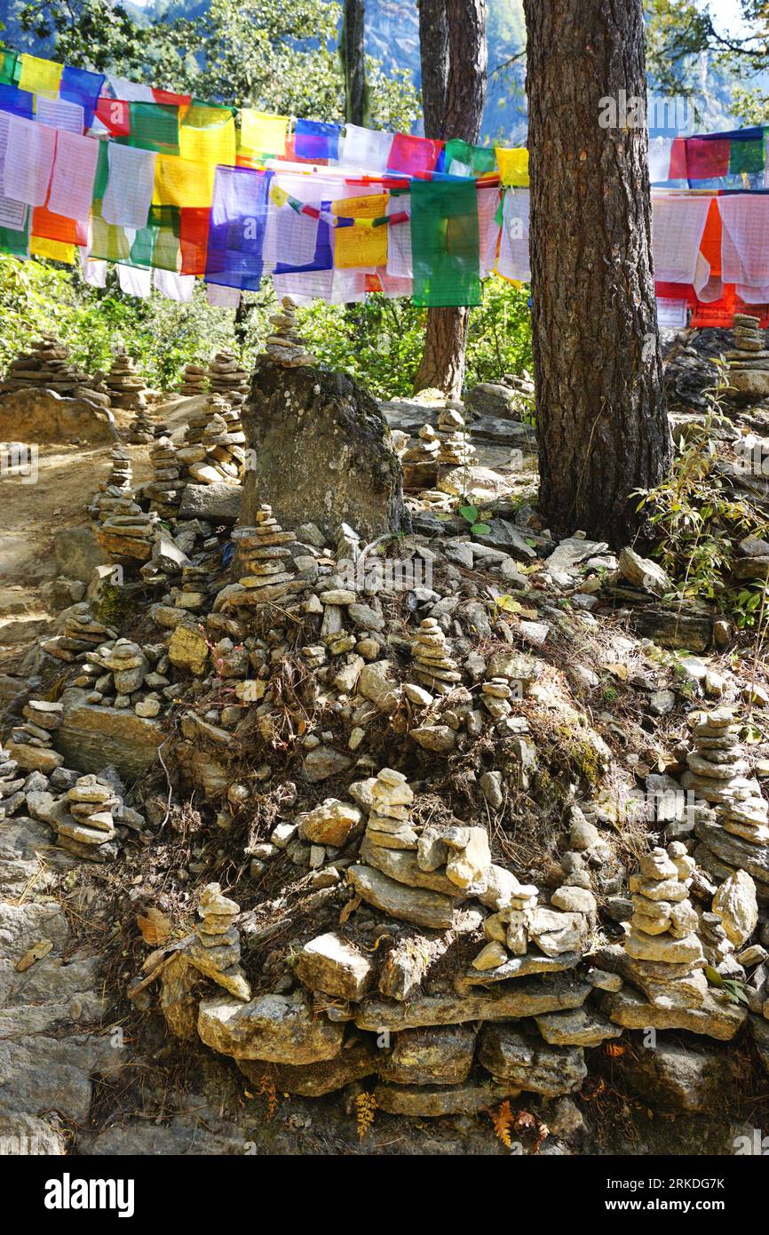 Stacked stone cairns fill the foreground while colorful prayer flag banners form a backdrop along the rugged trail to Bhutan's Tiger's Nest Monastery Stock Photo