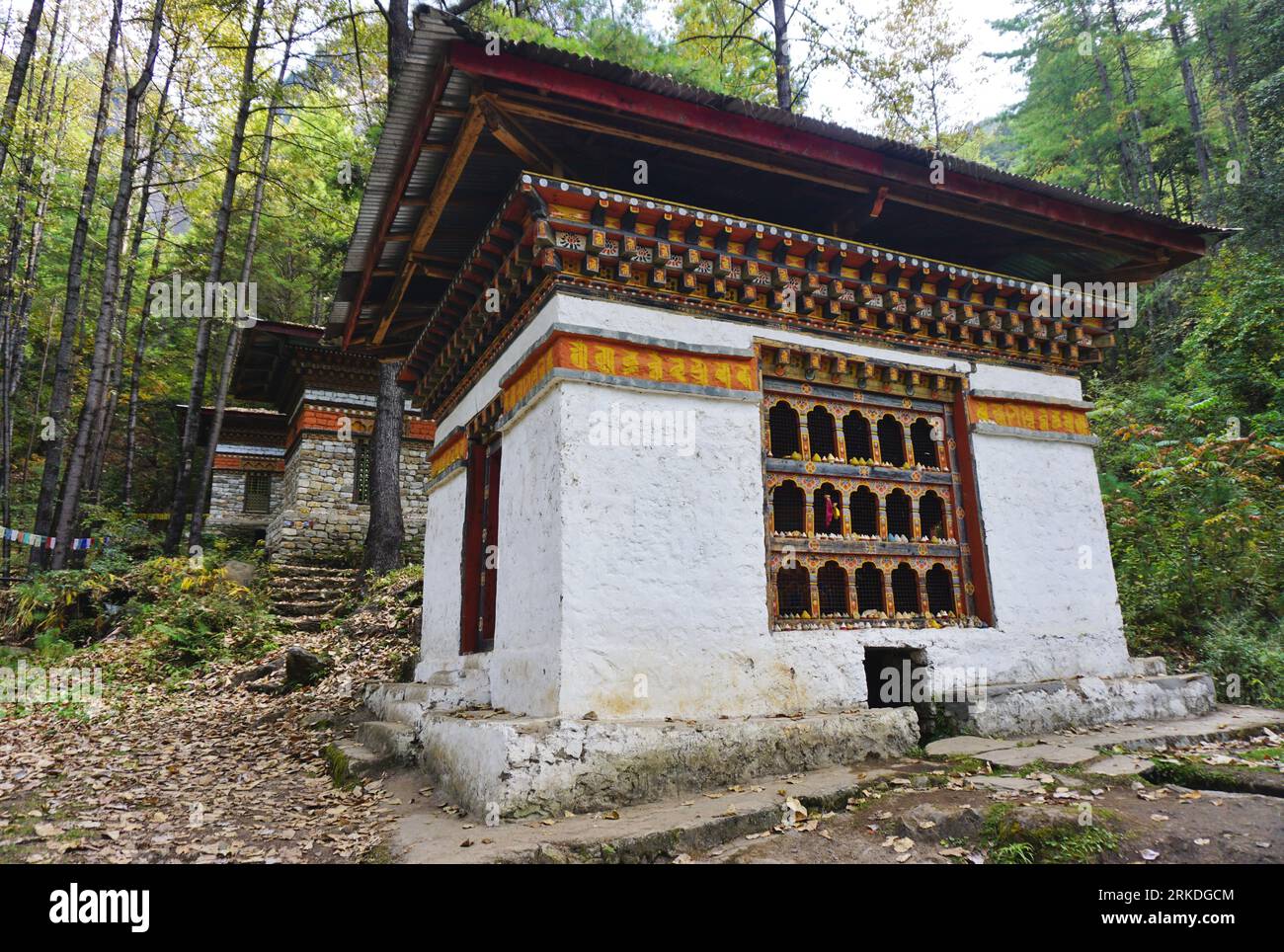 Three traditional stone buildings with typical Bhutanese painted woodwork house huge prayer wheels turned by water from a cascading mountain spring Stock Photo