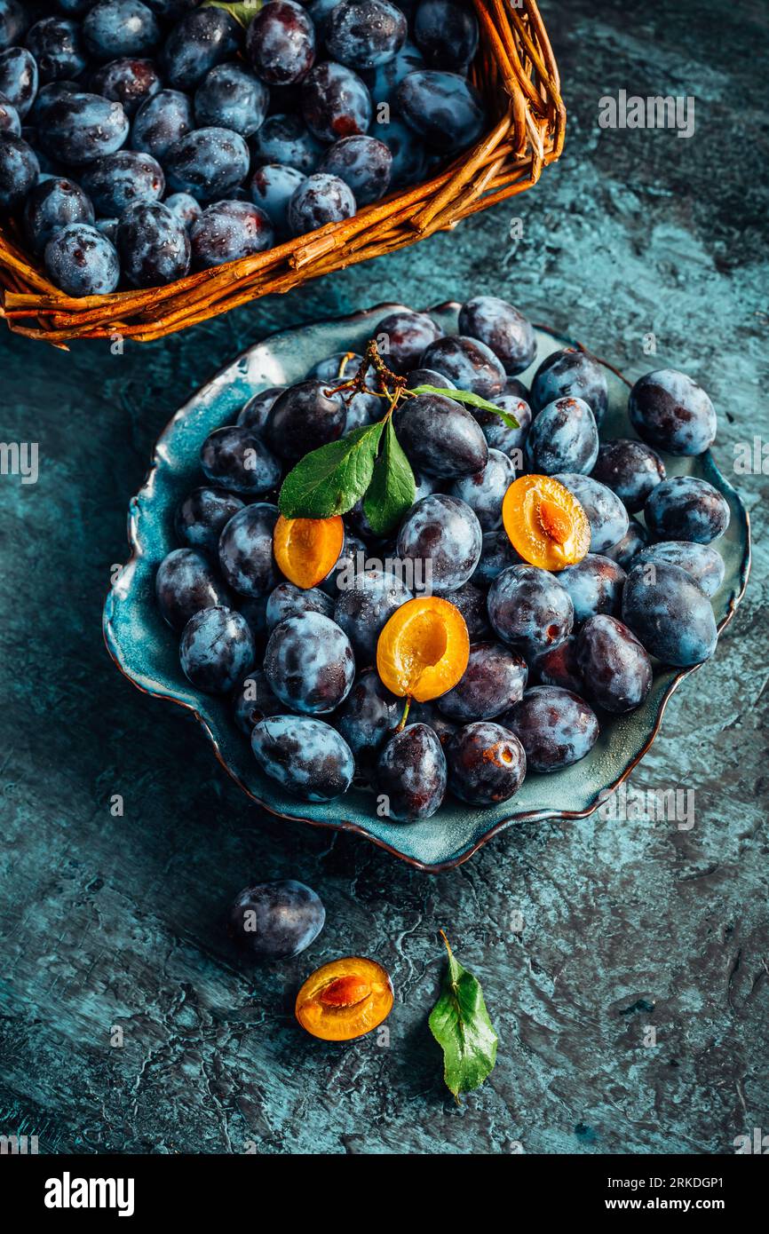 Freshly picked plums in a bowl and basket. Organic food and harvesting concept Stock Photo