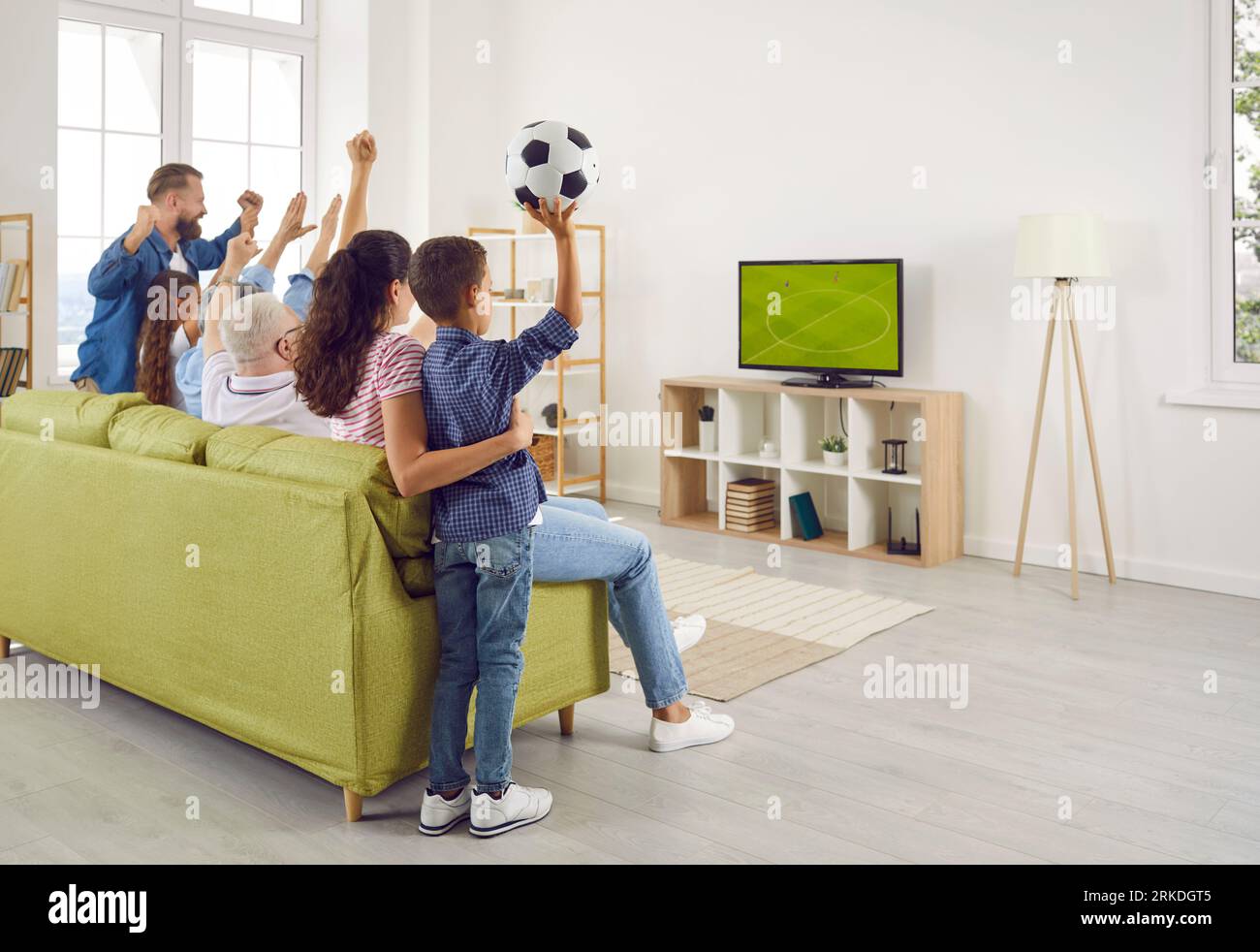 Happy, excited family sitting on couch in living room and watching football match on TV Stock Photo