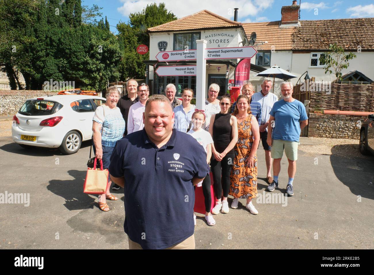 EDITORIAL USE ONLY Postmaster, Mark Eldridge with customers, unveiling a sign outside his Post Office in the rural village of Great Massingham, Norfolk, highlighting they provide the only cash services available in an 11-mile radius. Issue date: Friday August 25, 2023. Stock Photo