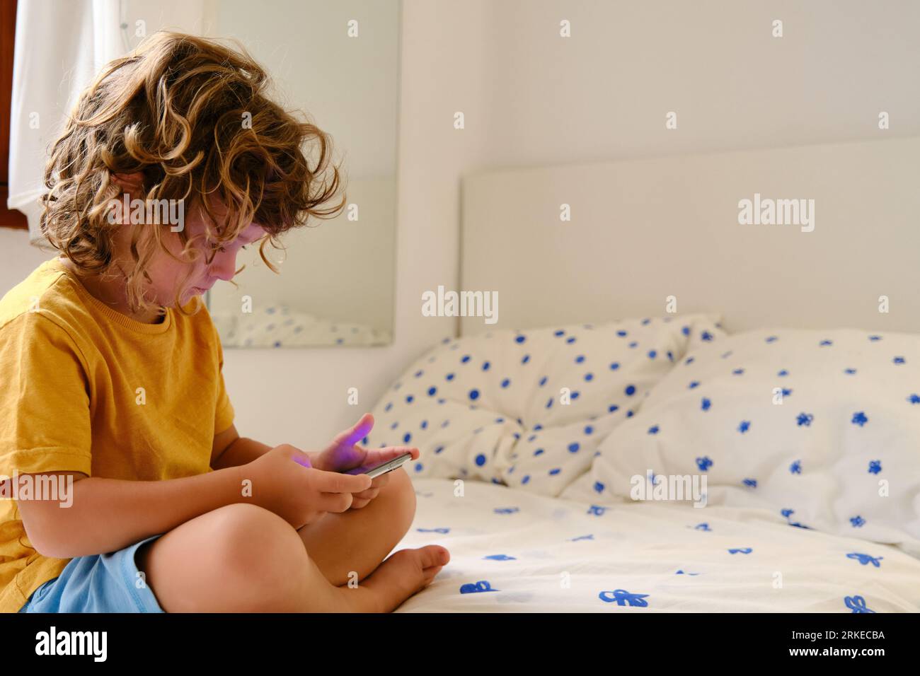 Boy with smartphone sitting on bed Stock Photo