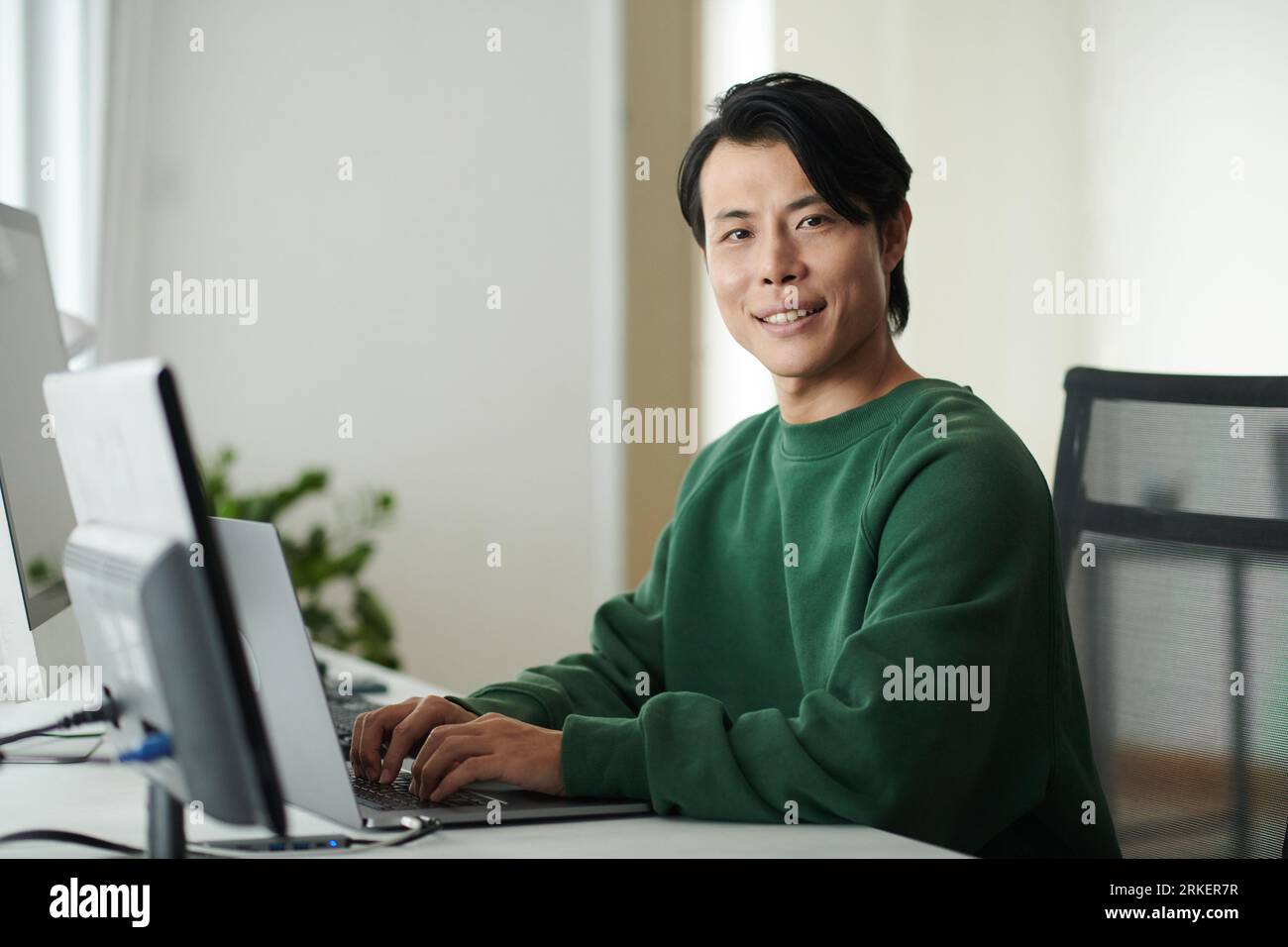 Portrait of smiling software developer working on computer and smiling at camera Stock Photo
