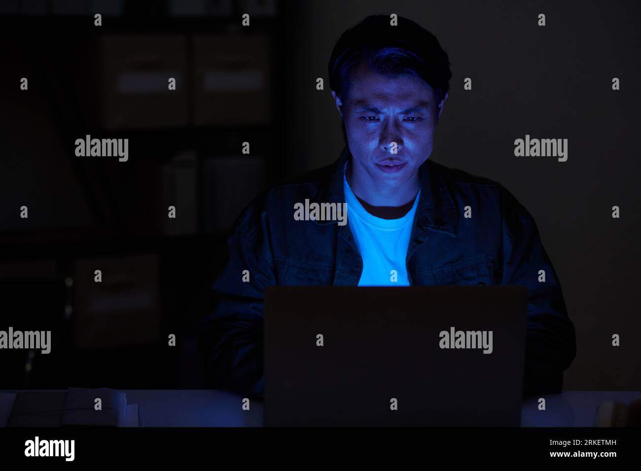 Portrait of serious software developer working on laptop in dark room ...