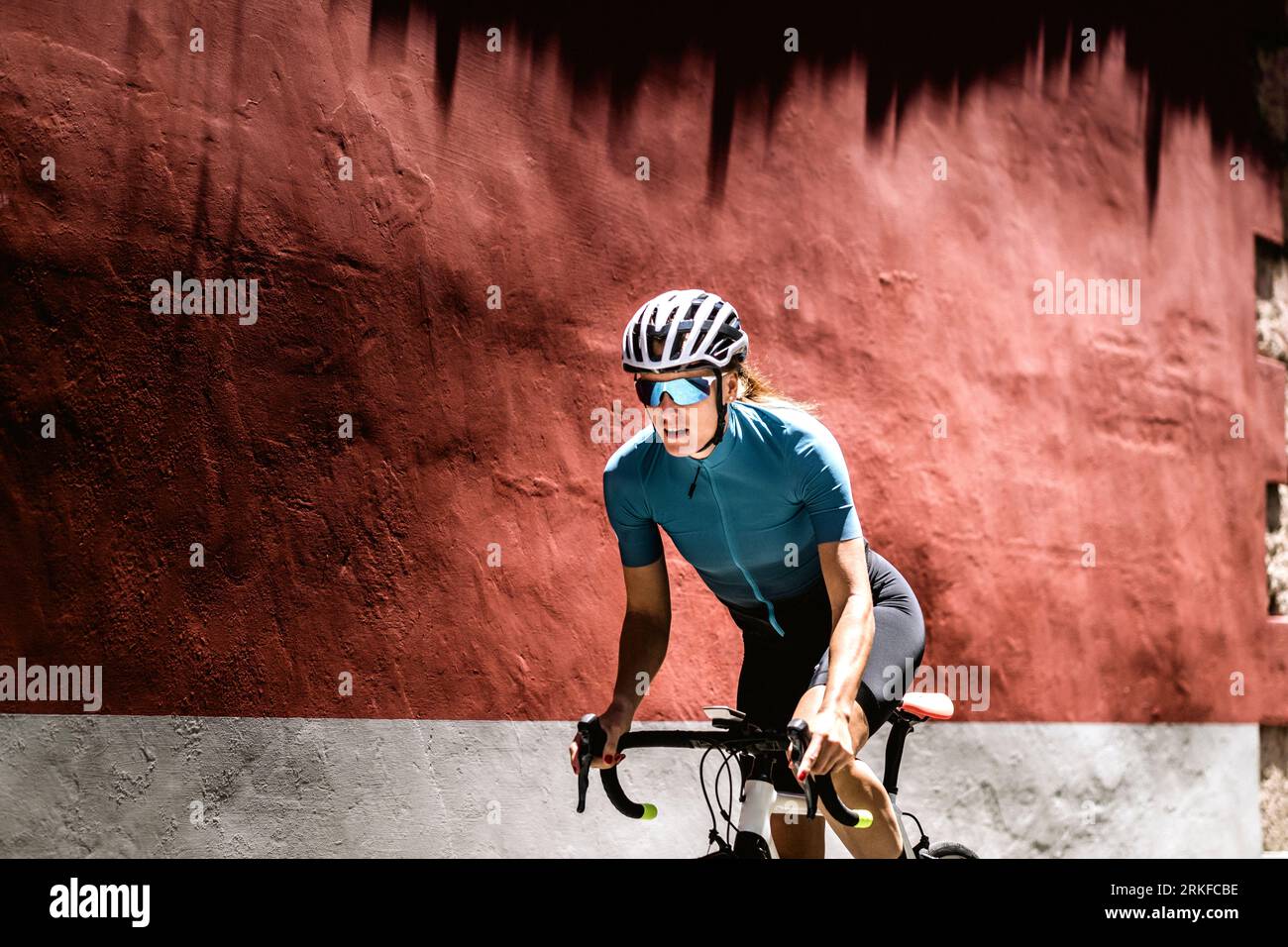 Female cyclist rides a bike against red wall backdrop Stock Photo - Alamy