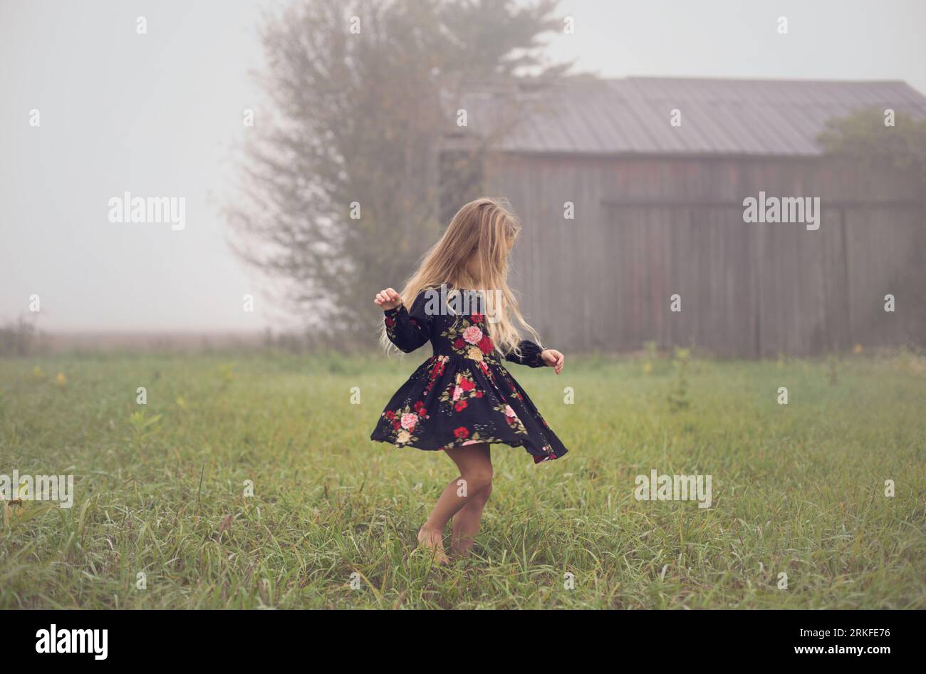 Young girl twirls alone on a foggy morning in an abandoned farm field Stock Photo