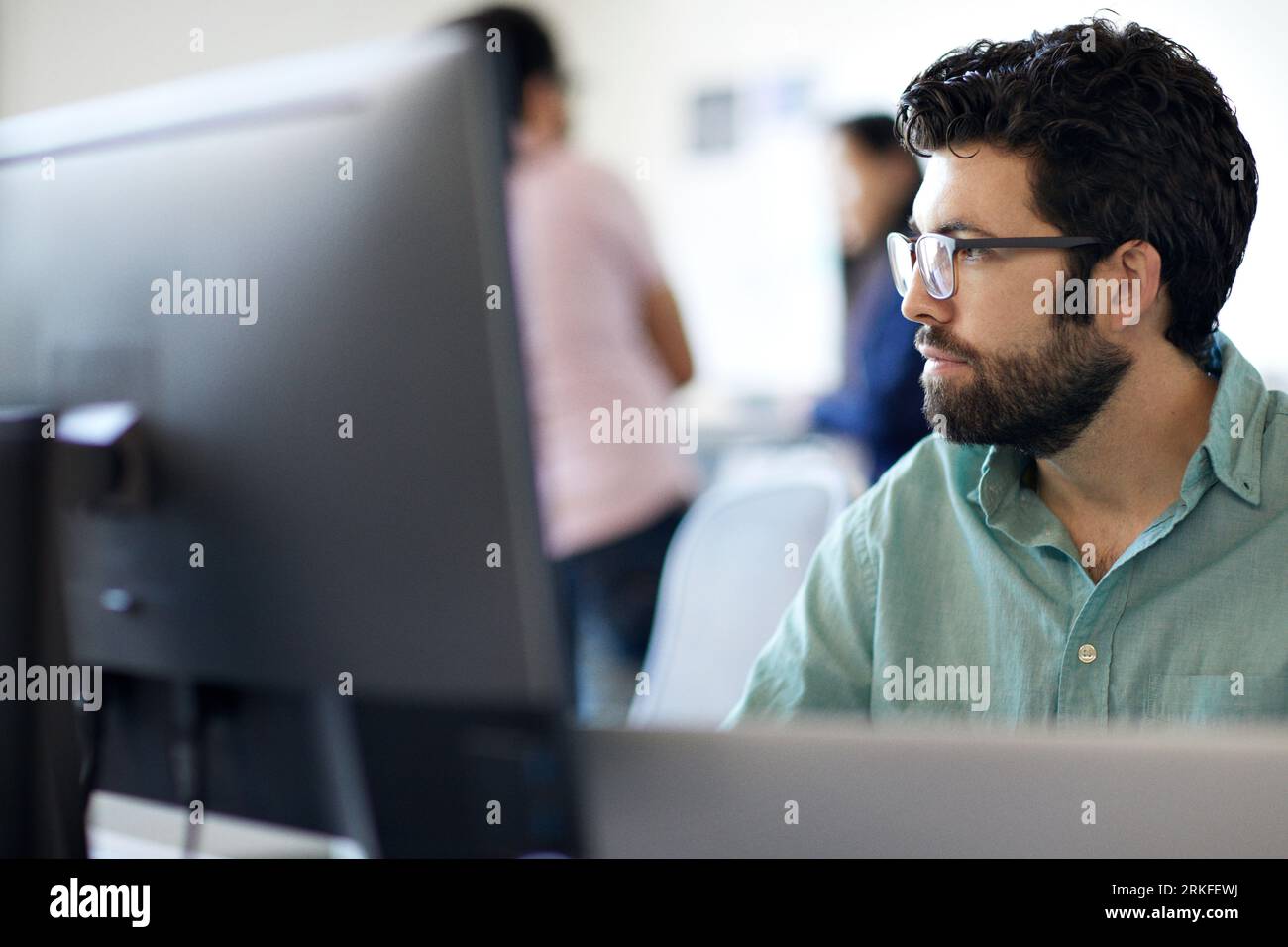 Close-up of bearded businessman using desktop computer while colleagues working in background at office Stock Photo