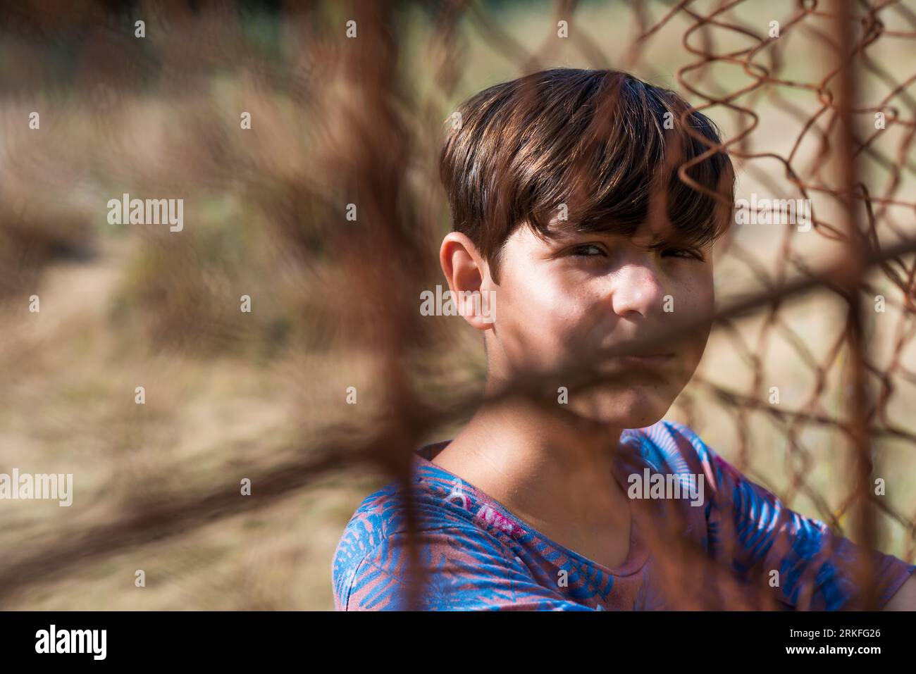 serious teen in casual wear behind metallic fence outdoors Stock Photo