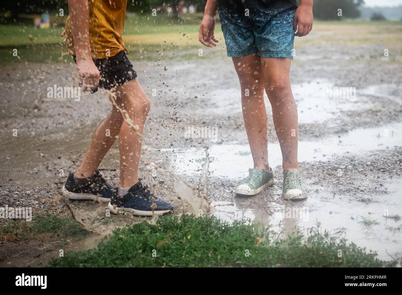 Kids splashing in mud puddle in the rain Stock Photo