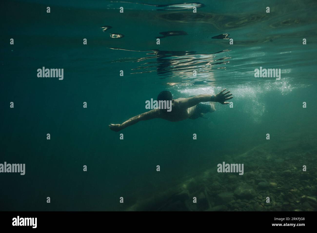 A young male dives underwater in a lake. Stock Photo