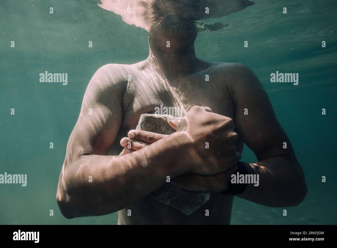 A young male holds a cement brick underwater. Stock Photo