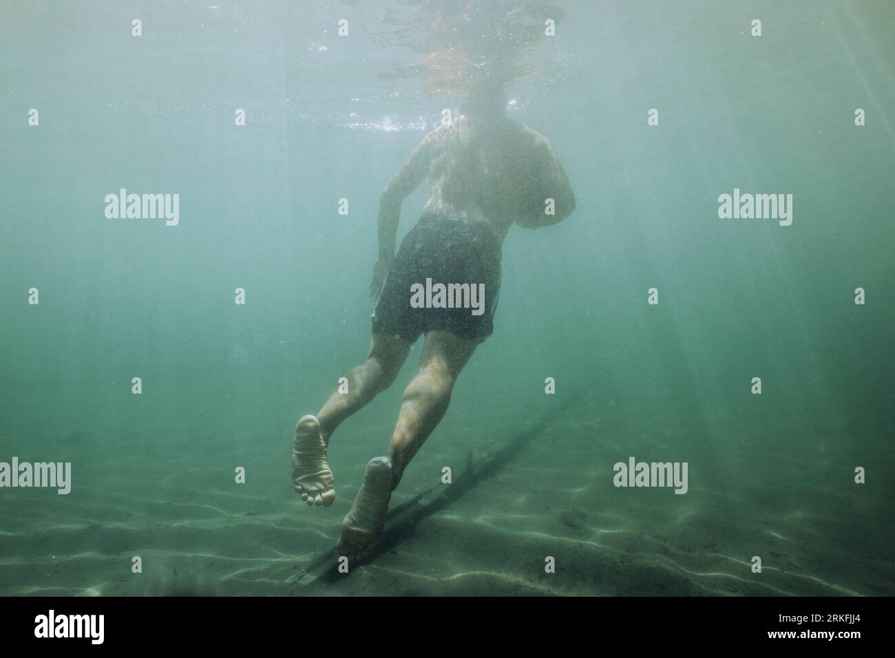 A young male floats freely underwater in a lake. Stock Photo