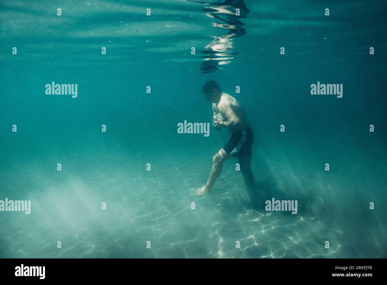 A young male walks across sand underwater. Stock Photo
