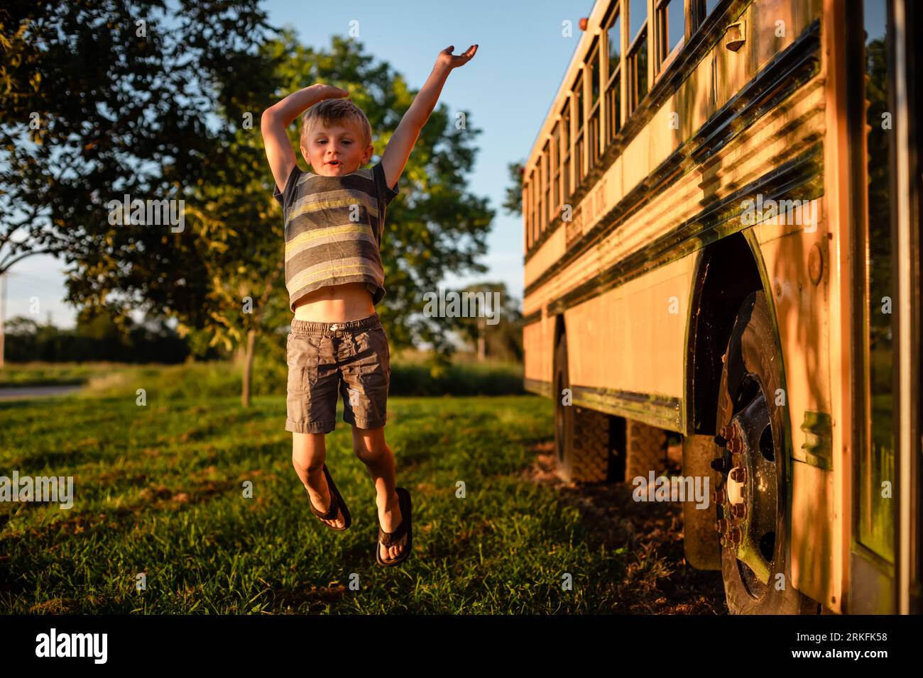Young child jumping for joy next to school bus during back to sc Stock