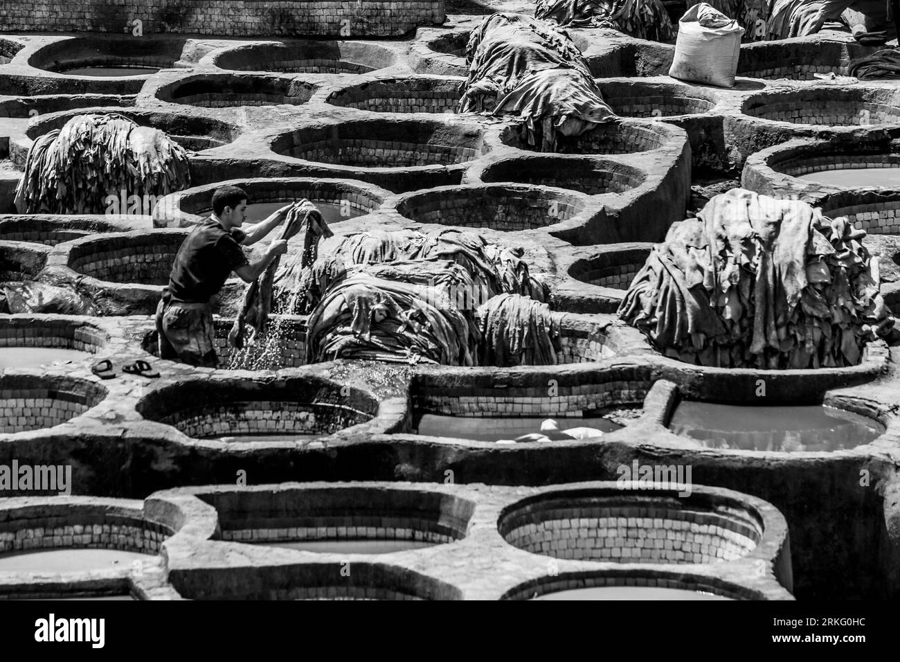 Men working at the Chouara Tannery in Morocco, putting leather in round stone vessels to soften and dye it in different colours. At Fez el Bali Stock Photo