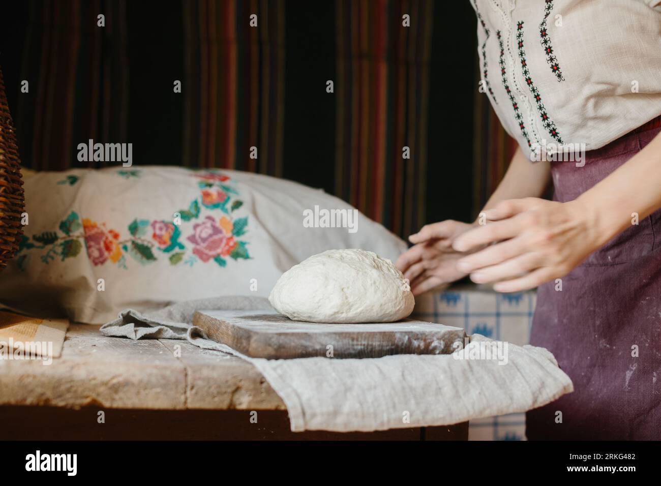 A woman in national Ukrainian embroidery kneads dough for bread. Stock Photo