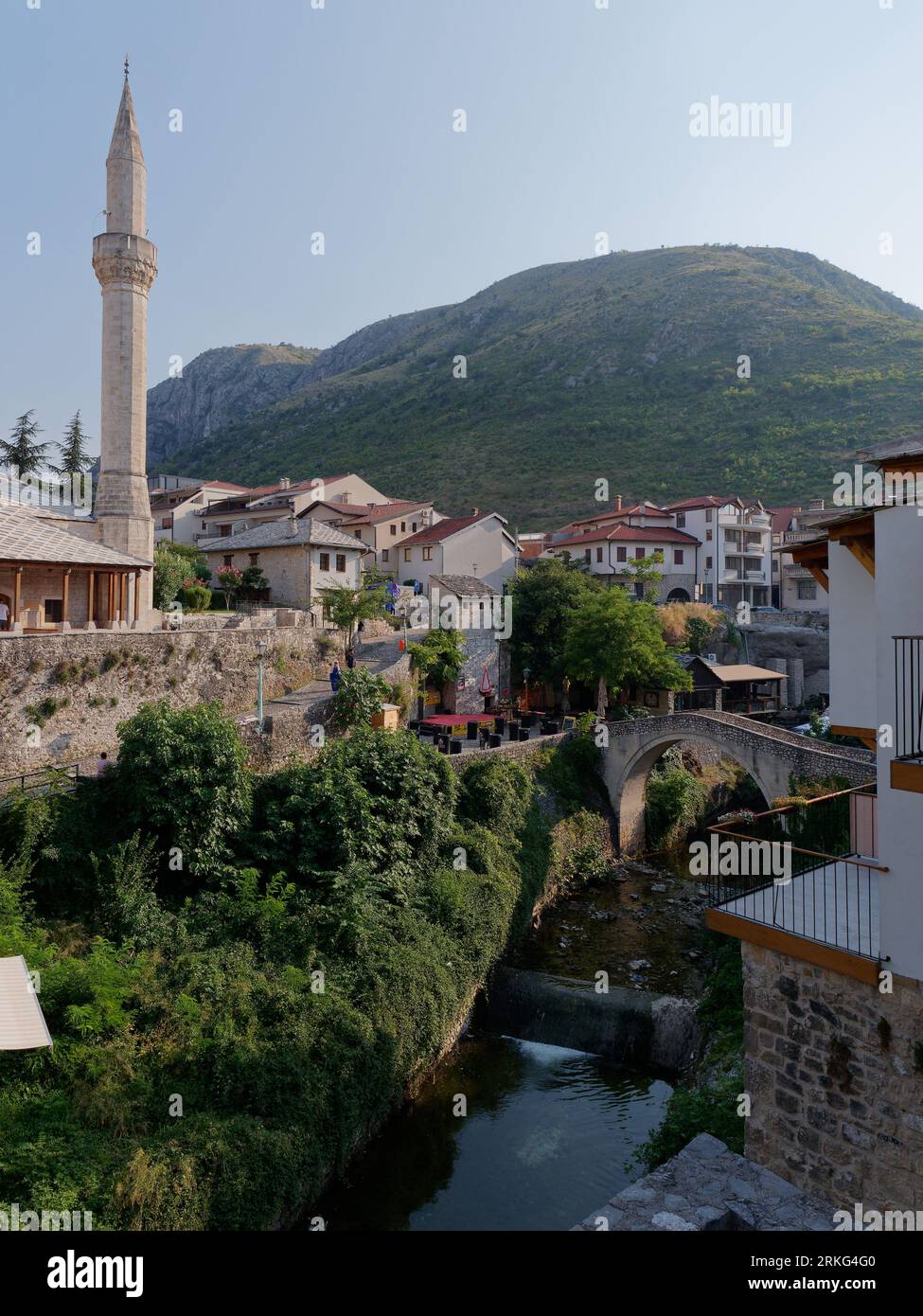 Hadži Kurt Mosque exterior surrounded by houses and mountains and a bridge over the River Nervetva,  Mostar, Bosnia and Herzegovina, August 21, 2023. Stock Photo