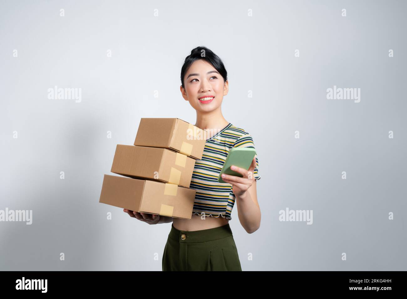 Young happy asian woman wear summer casual clothes hold stack cardboard blank boxes use mobile cell phone Stock Photo