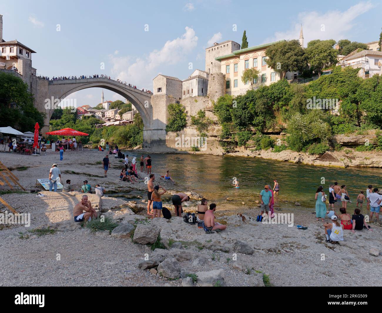 People on a beach along the River Neretva with Stari Most (Old Bridge) behind in the city of Mostar, Bosnia and Herzegovina, August 21, 2023. Stock Photo