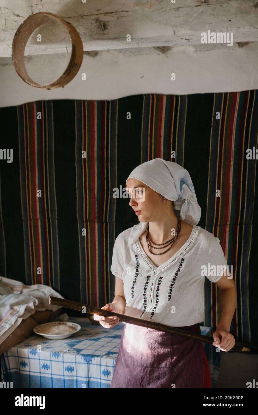 A woman in Ukrainian national dress works near a woodburning stove