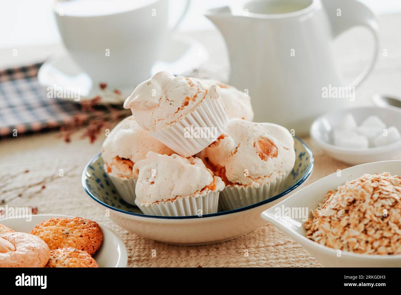 a ceramic bowl with some spanish merengues almendrados, baked meringues with almonds, on a table next to a white ceramic plate with some cookies Stock Photo