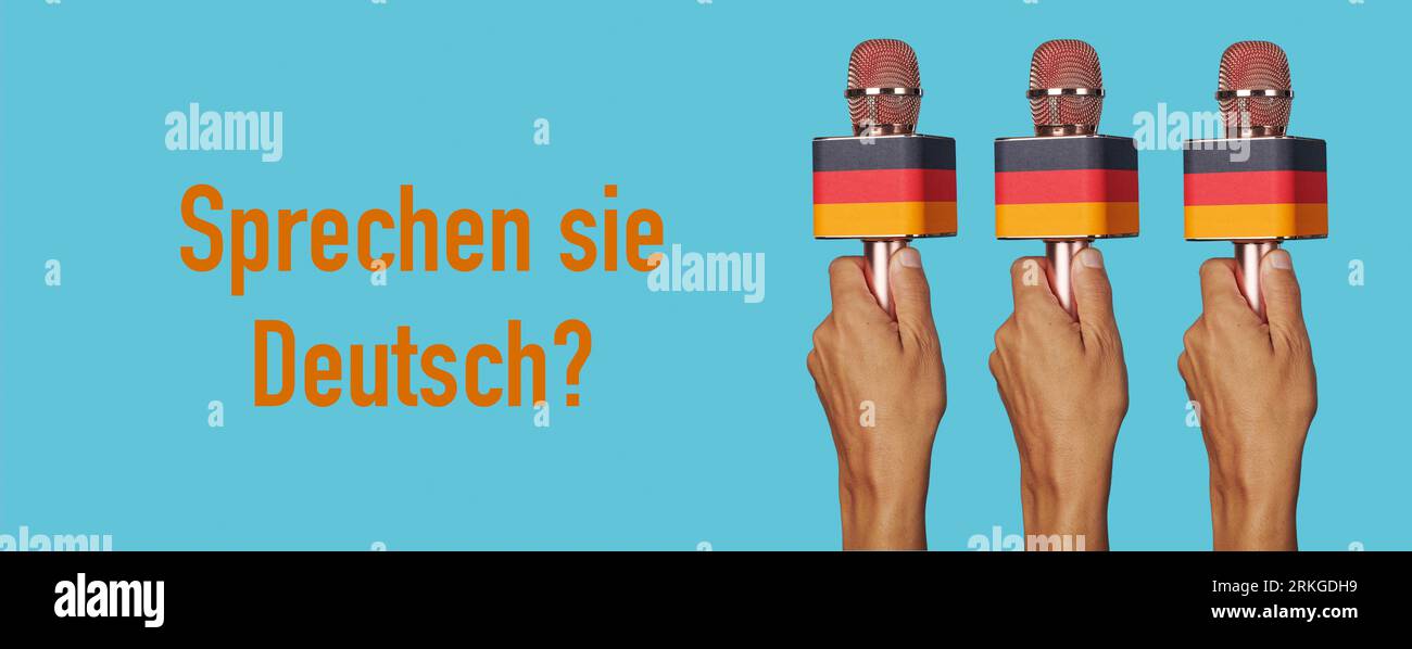 man hands holding microphones patterned with the german flag and the question do you speak german written in german in a panoramic format to use as we Stock Photo
