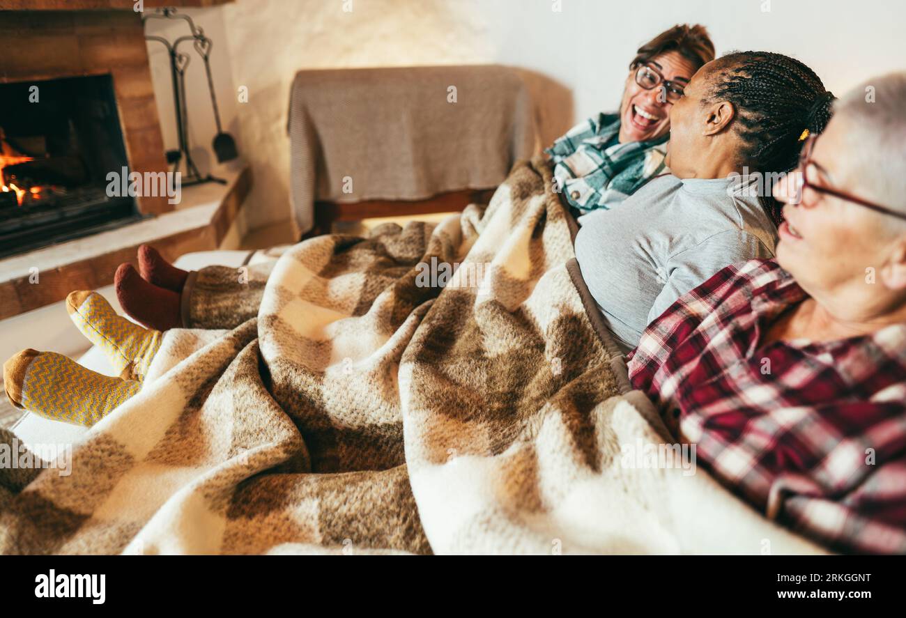 Multiracial women relaxing at home chalet in front of fireplace during winter time - Cozy time with friends concept - Main focus on african female fac Stock Photo