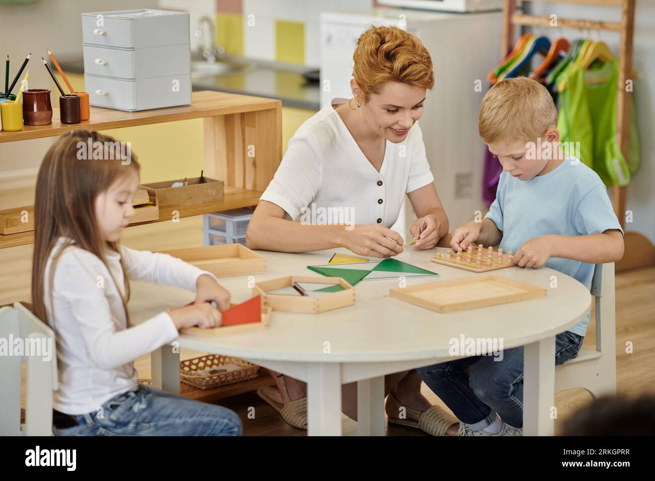 smiling teacher playing with kids and didactic materials on table in