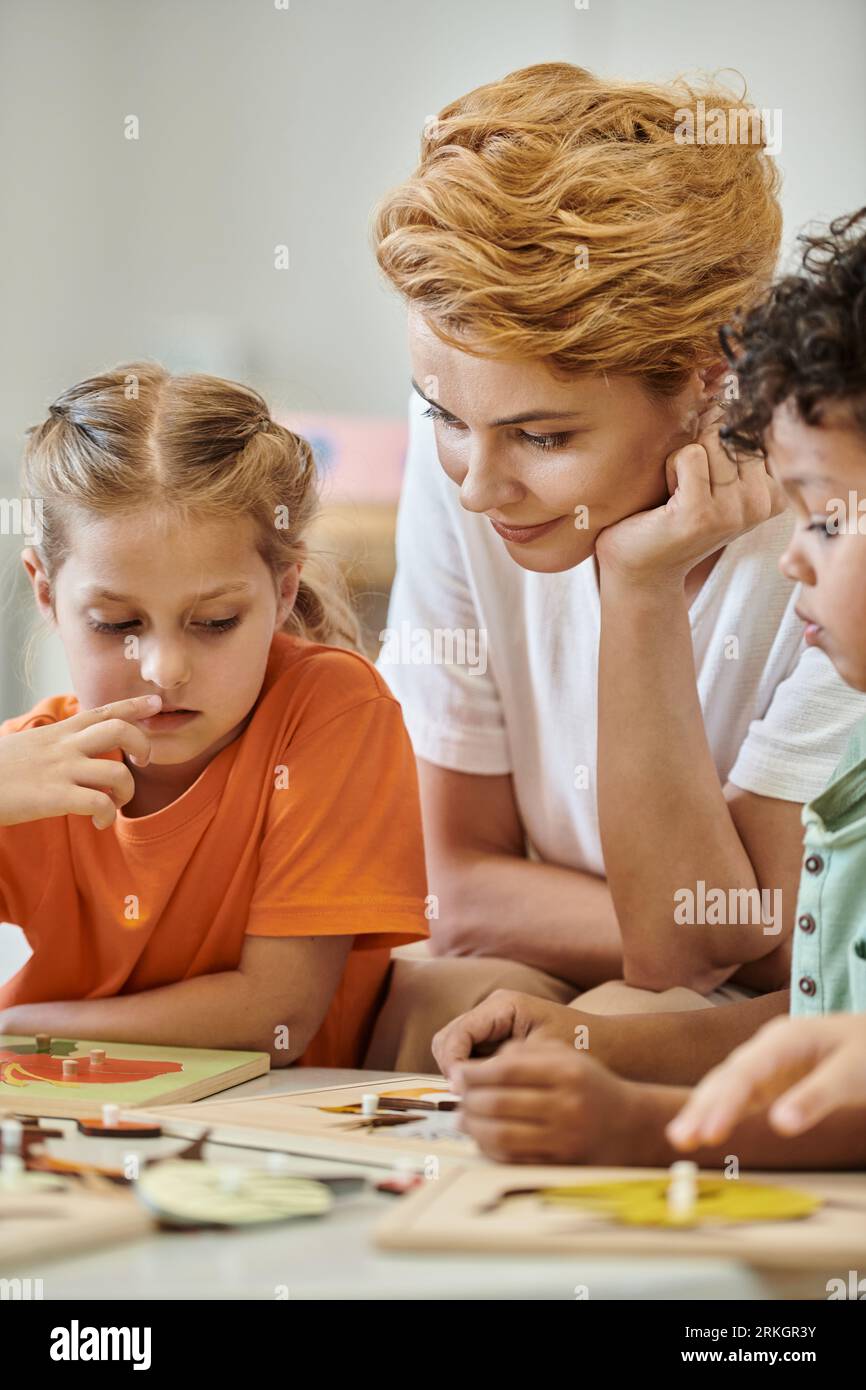 kid talking to teacher near child and didactic material in montessori