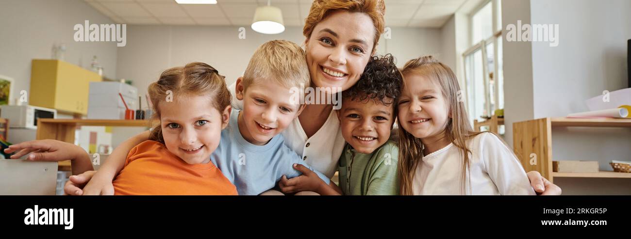 cheerful teacher and interracial kids looking at camera during lesson ...