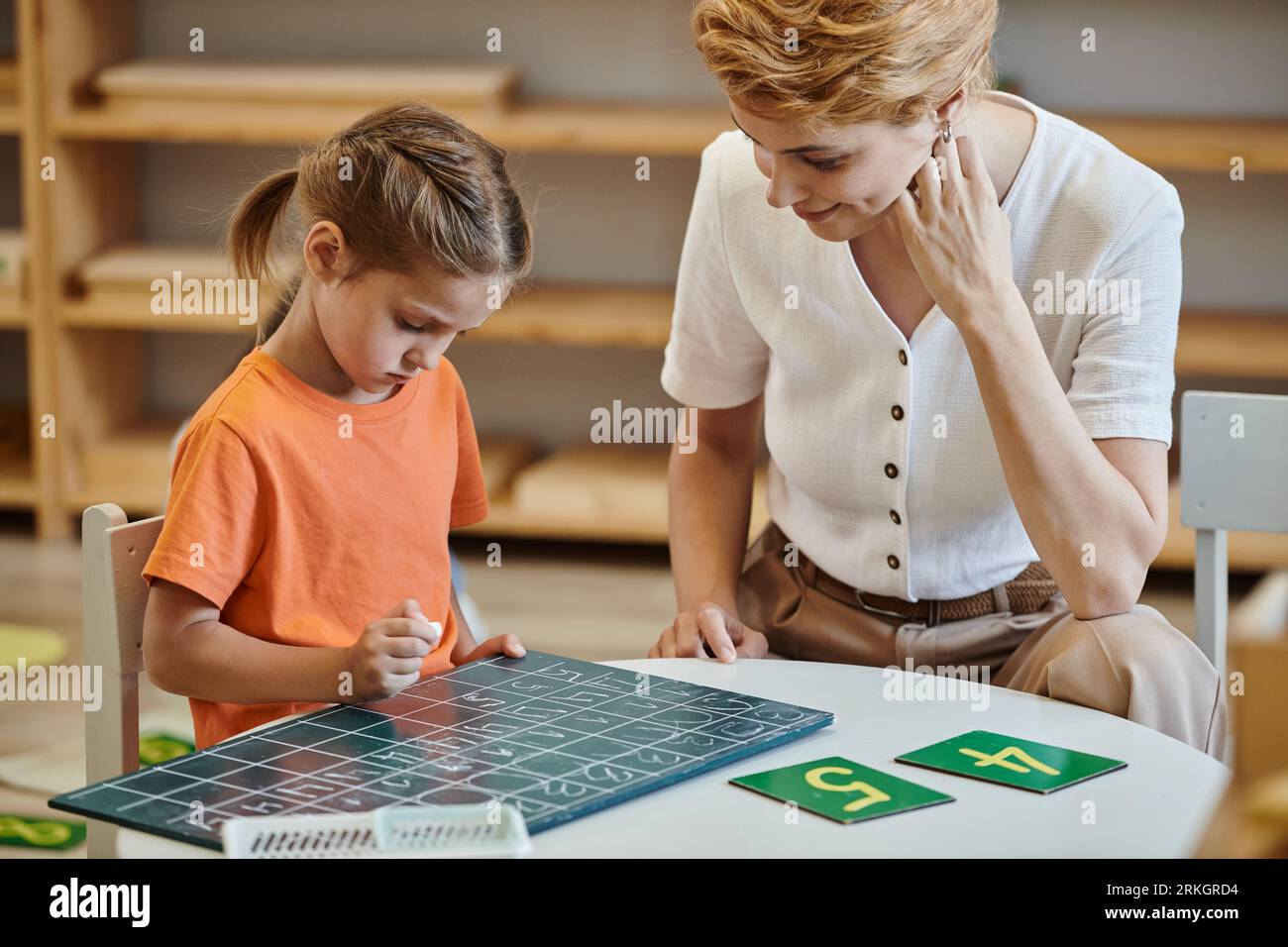 cute girl looking at chalkboard near numbers, learning through play
