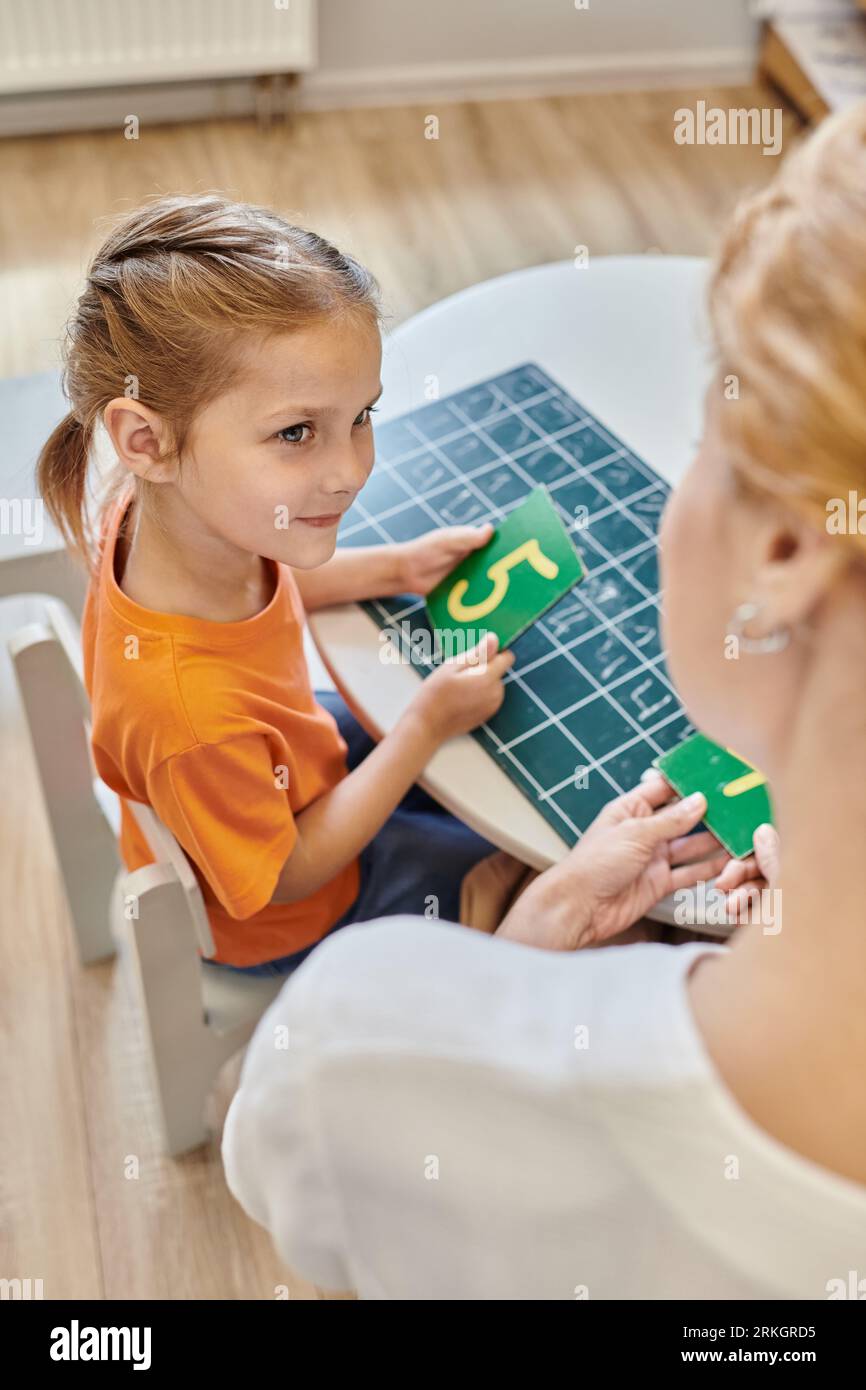 clever girl and teacher holding numbers near chalkboard, learning