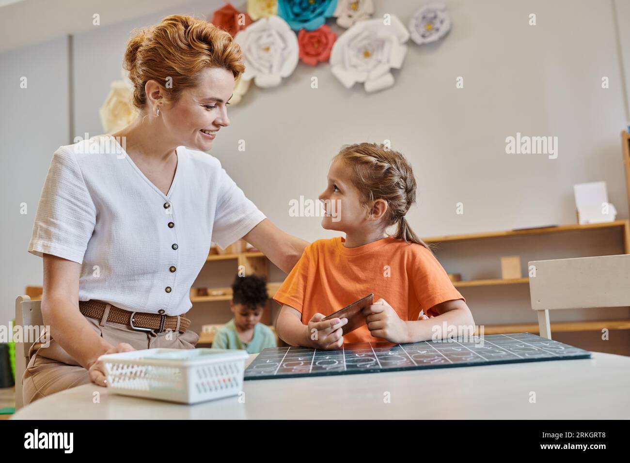 happy teacher encouraging smart girl in Montessori school, learning through play, counting, math Stock Photo