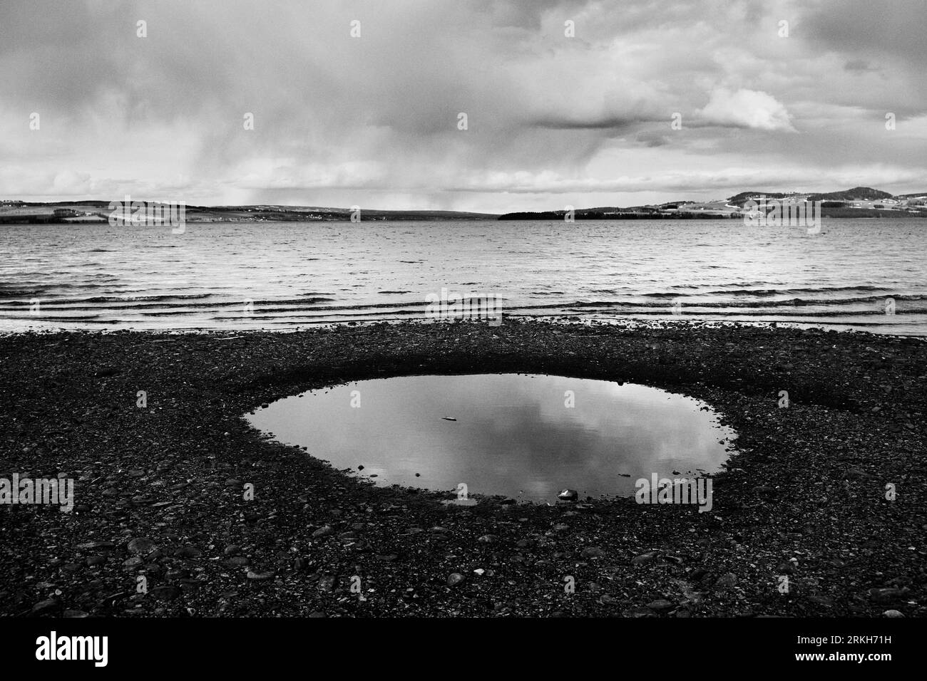 A puddle of water in front of a majestic and vast ocean in grayscale