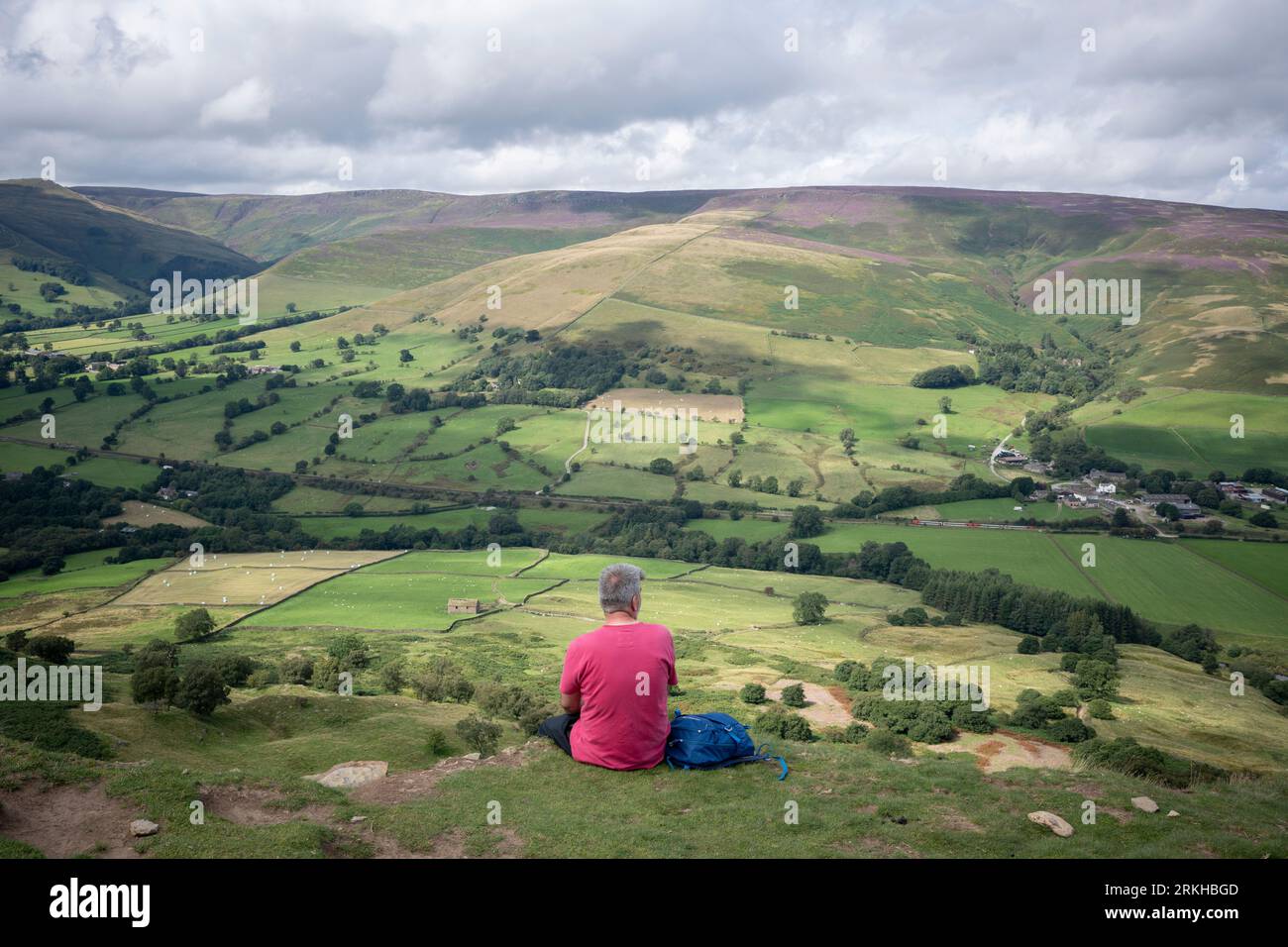 A man rests at Hollins Cross and overlooks a landscape of fields and farming land in Edale Valley in the Peak District National Park, on 23rd August 2023, in Sheffield, England. Stock Photo