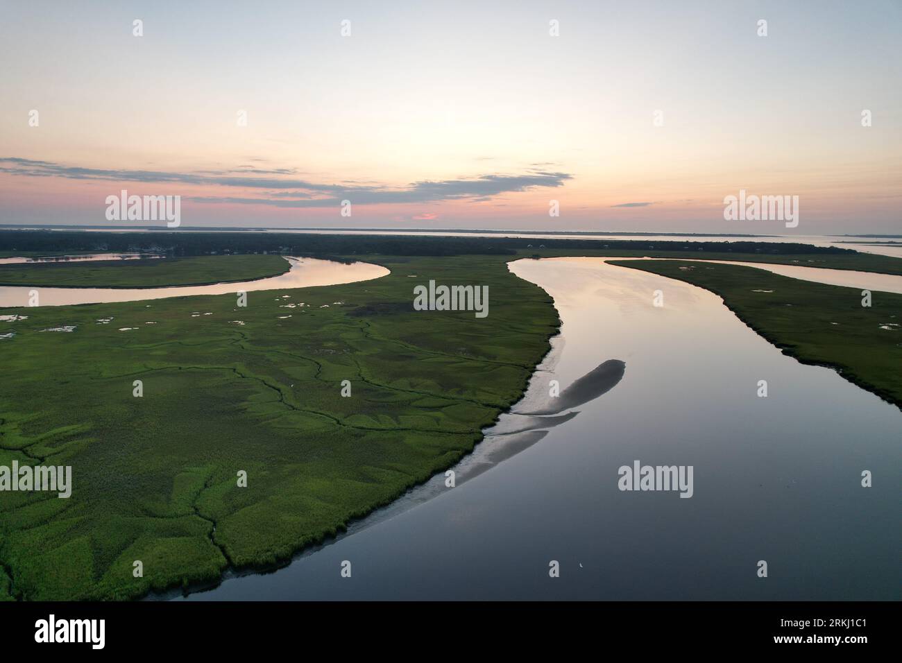 An aerial view of a river flowing through a green landscape at sunset ...