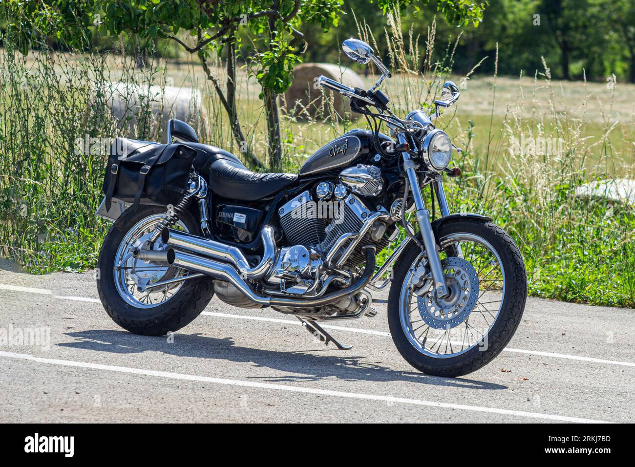 A black Yamaha Virago motorcycle parked surrounded by  lush green on  a sunny day Stock Photo