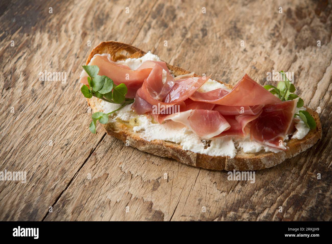 An example of bruschetta made with toasted sourdough bread, ricotta cheese and Serrano ham. Drizzled with olive oil and garnished with watercress. Pre Stock Photo