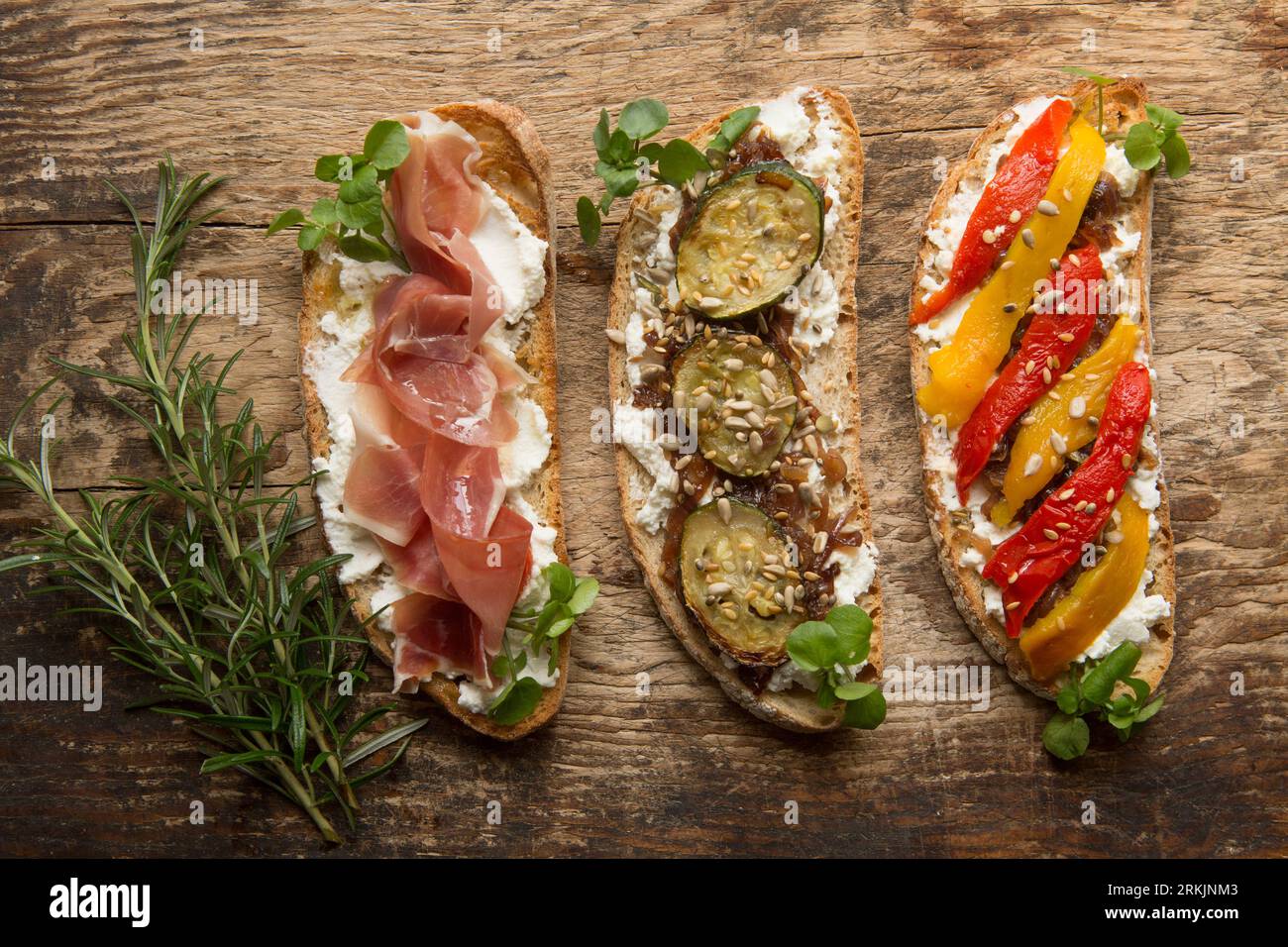 Three examples of bruschetta made with toasted sourdough bread spread with ricotta cheese. The toppings left-right are: Serrano ham drizzled with oliv Stock Photo